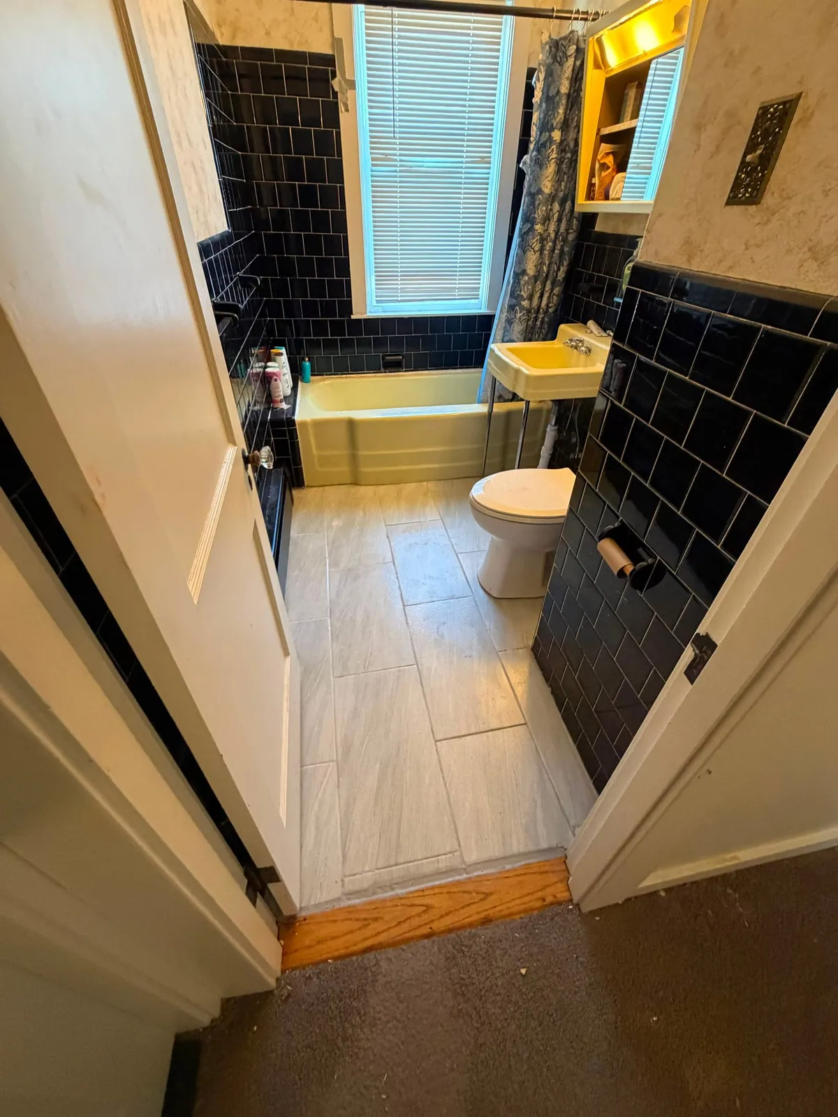 Bathroom with new finished flooring installed against black tile walls